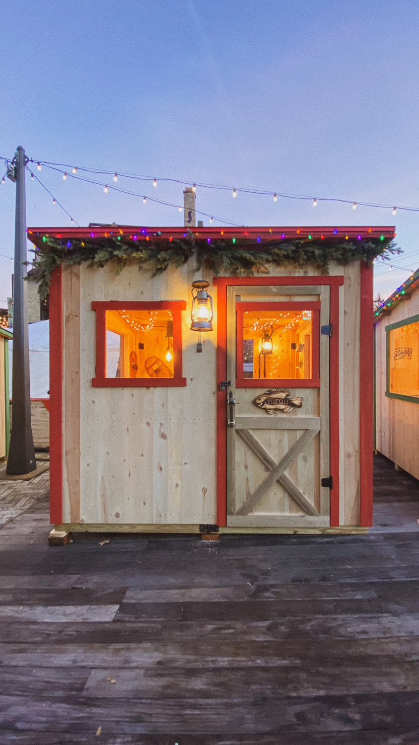 A shanty lined with red paint, pine garland, and christmas lights